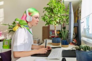 Una donna adulta con capelli scuri, seduta davanti al computer con una pianta sulla sua destra, indossando cuffie sulla testa mentre lavora sulla tastiera, è concentrata nella cura dellipertensione oculare primaria