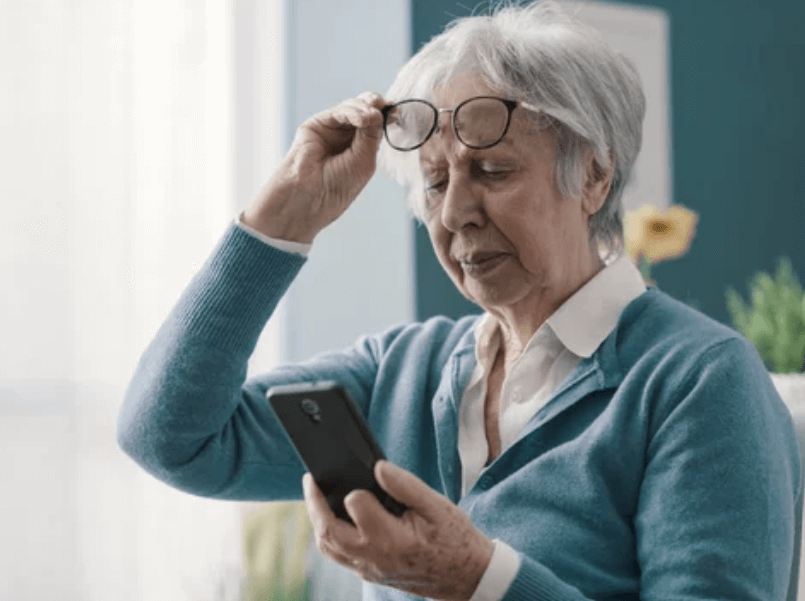 Donna anziana che non vedendo bene il suo telefono si toglie l'occhiali