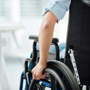 Una persona con distrofia muscolare congenita che utilizza FootMobili per spostarsi in sedia a rotelle La sedia è dotata di un braccio meccanico per aiutare nei movimenti, mentre le ruote e il piede della macchina consentono di spostarsi facilmente