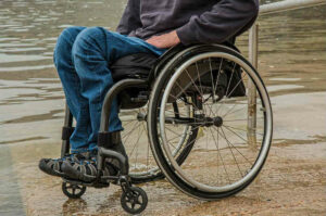 Una persona con una malattia neuromuscolare che si sposta con una sedia a rotelle munita di ruote, tra i mobili della macchina e la sedia una storia di speranza e di libertà